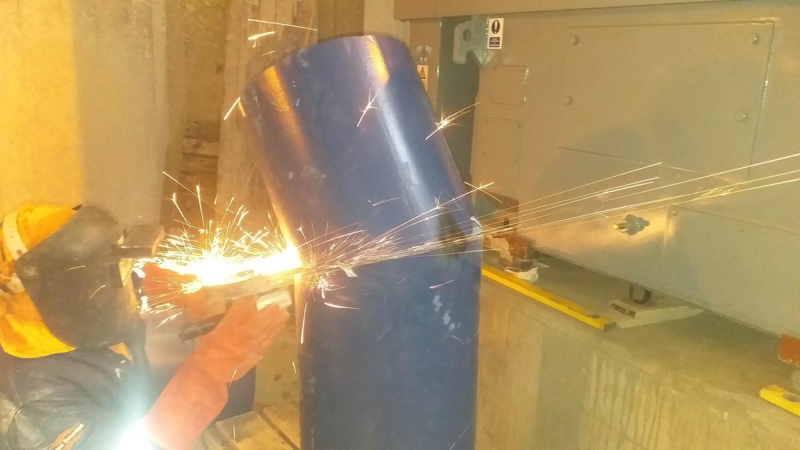 Technician using an angle grinder on a blue fabricated steel pipe fitting as sparks fly