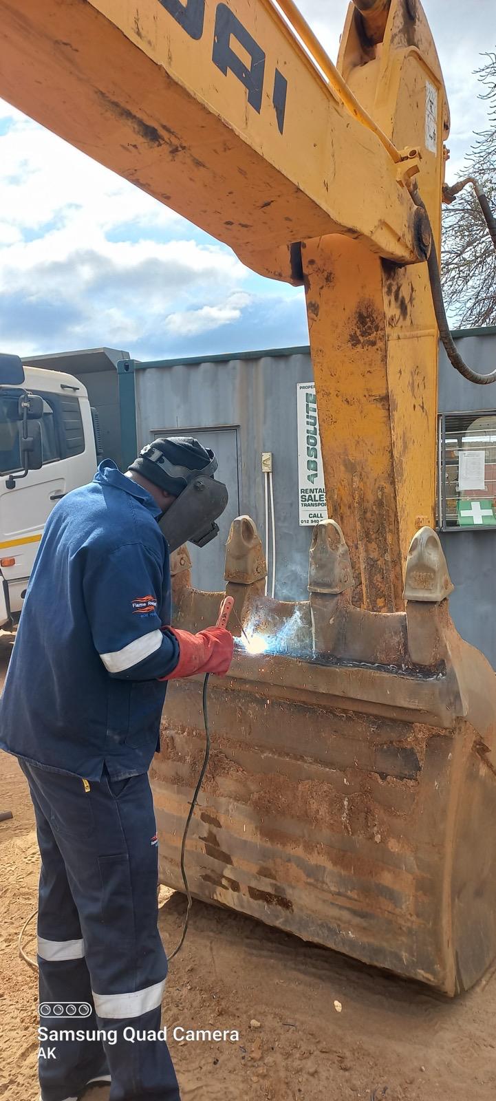 Welder repairing the steel edge of an excavator bucket on site