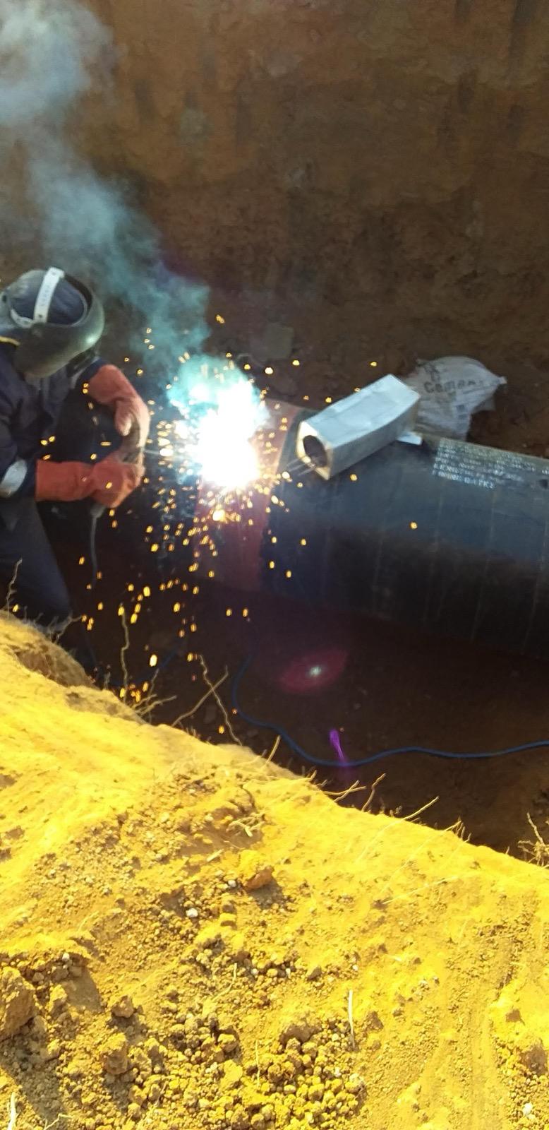 Welder joining a large-diameter steel pipeline in an excavated trench