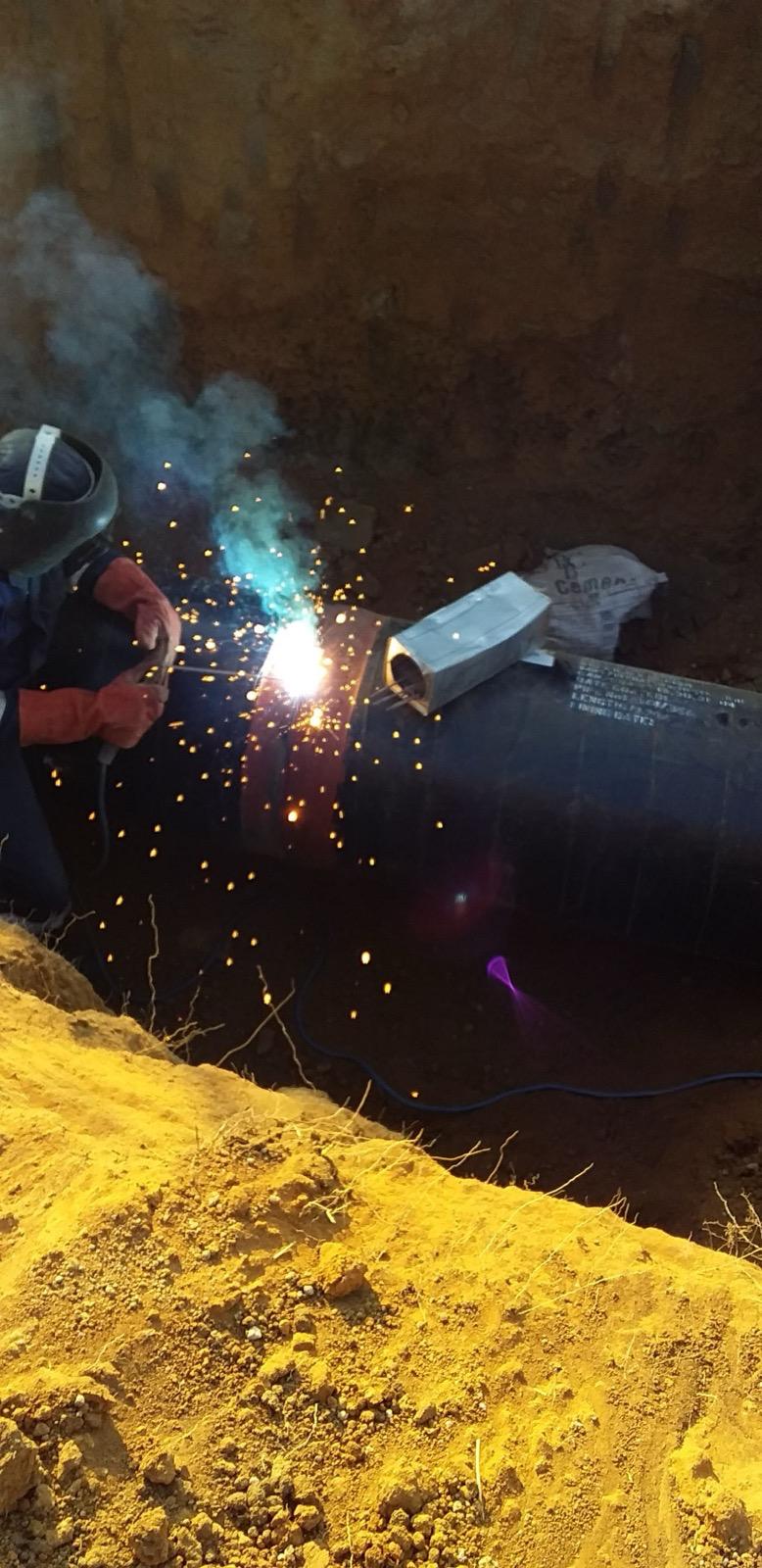 Pipeline welder completing a joint on a steel pipe in a trench