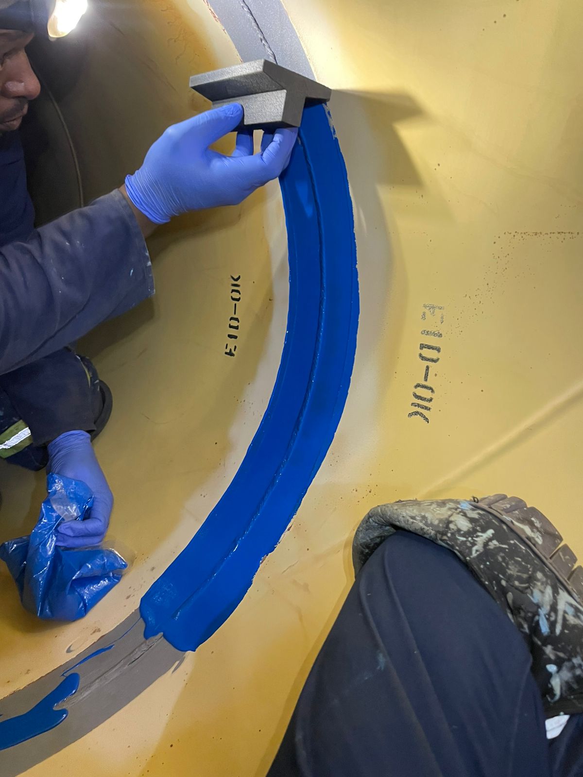 Team member applying and shaping blue coating over an internal pipe joint