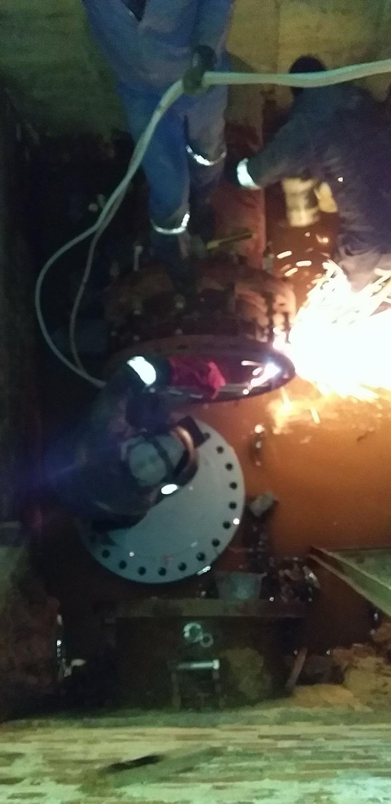 Technician using a power tool on a flanged pipeline connection in a dim plant area