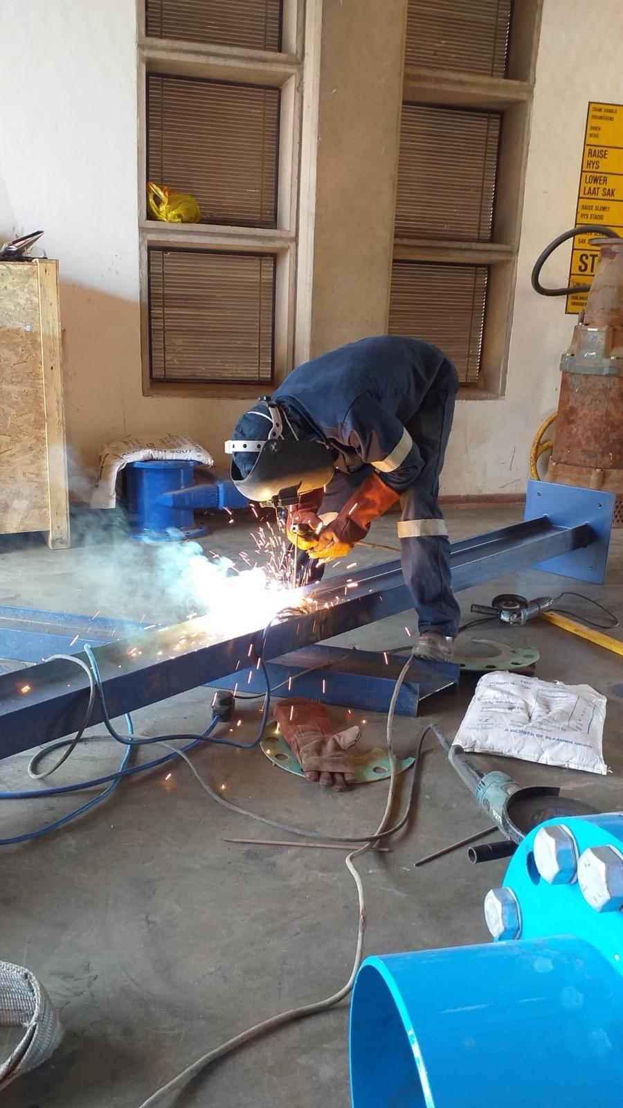 Fabricator using an angle grinder on a blue steel support frame in a workshop