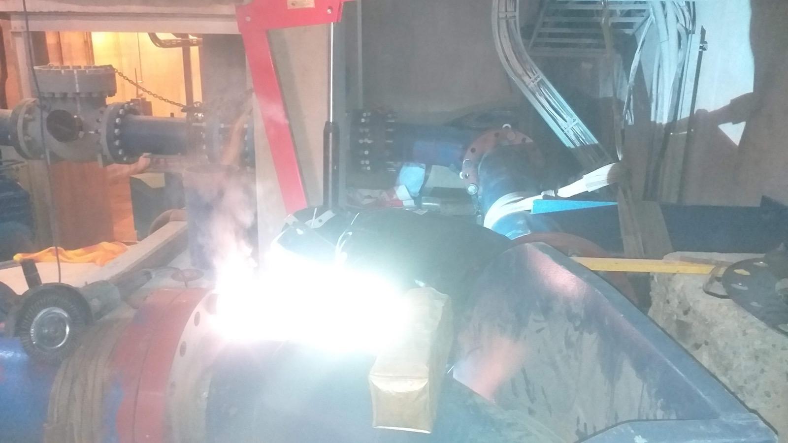 Bright welding arc on a large fabricated steel pipe fitting in a workshop